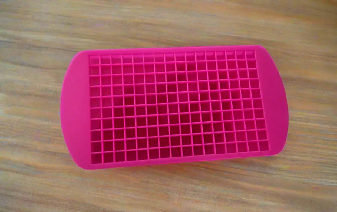 Pink silicone mold with small compartments held by a hand on a tiled floor.