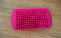 Pink silicone mold with small compartments held by a hand on a tiled floor.