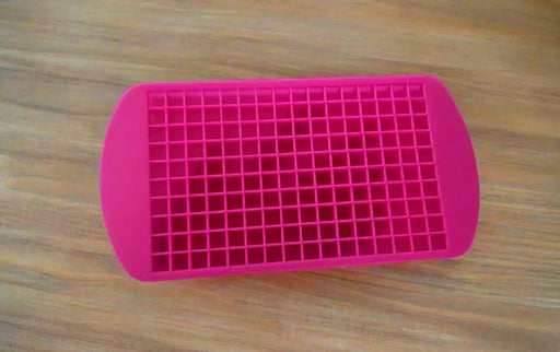 Pink silicone mold with small compartments held by a hand on a tiled floor.
