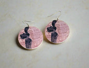 Two circular earrings with a design on a green surface.