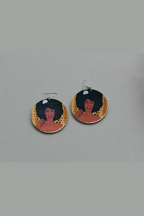 Pair of earrings with a woman's face design on a green surface.