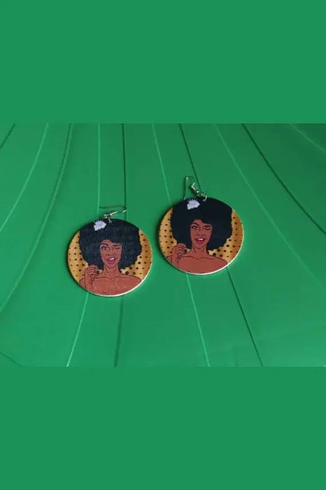 Pair of earrings with a woman's face design on a green surface.