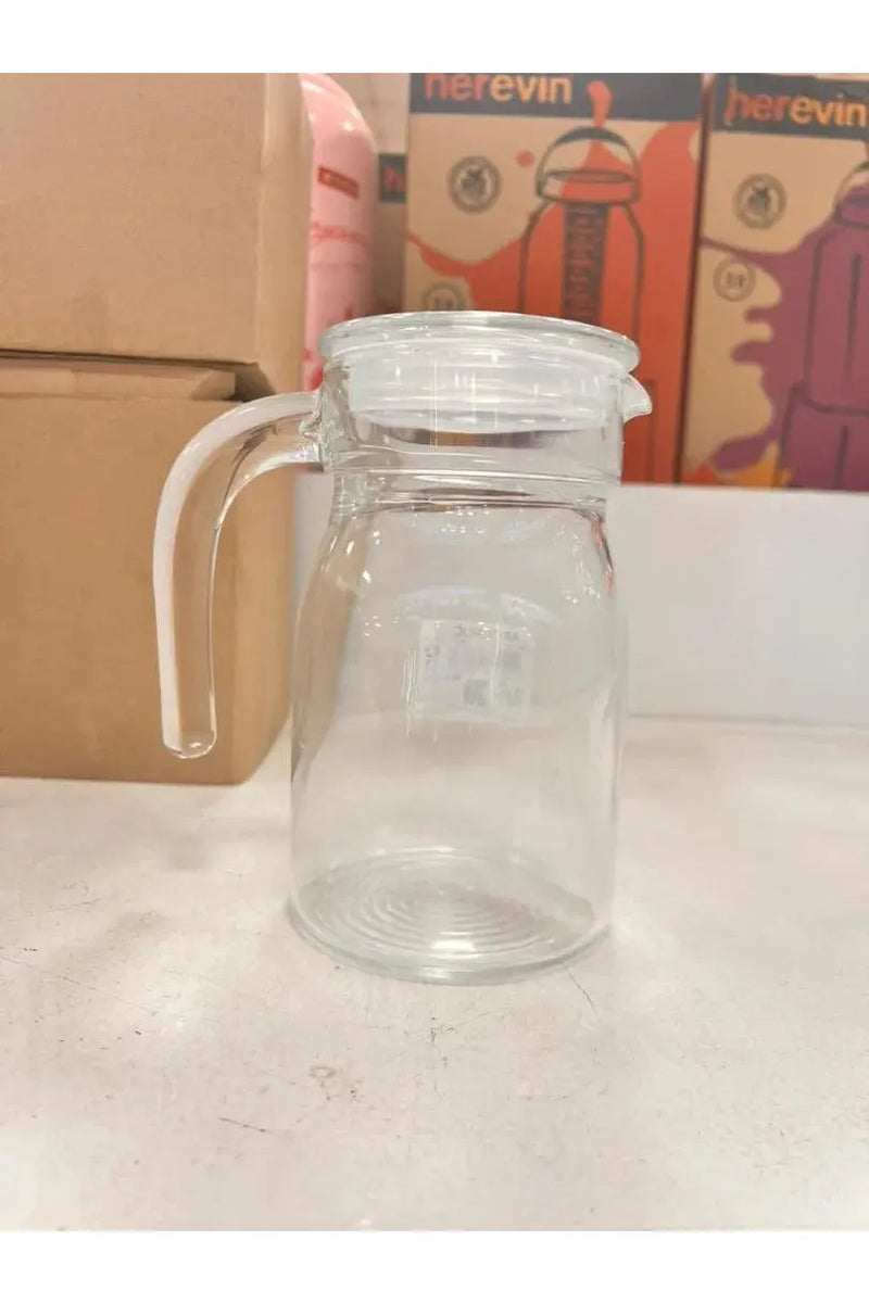 Clear glass jar with handle on a white surface with boxes in the background