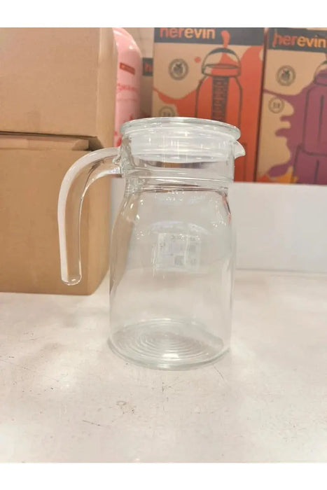 Clear glass jar with handle on a white surface with boxes in the background