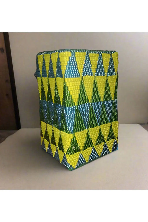 Handheld beaded container with green and yellow pattern, held by a hand.