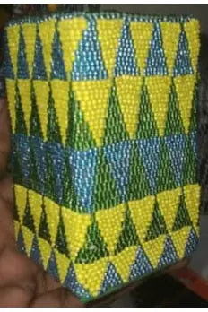 Handheld beaded container with green and yellow pattern, held by a hand.