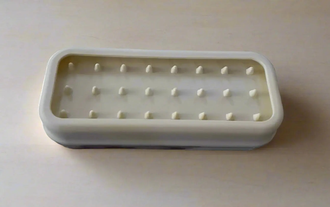 Rectangular white plastic tray with multiple small holes on a tiled floor.