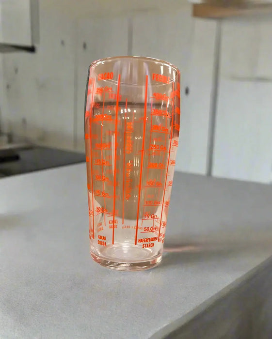 Clear measuring glass with orange measurements on a white surface