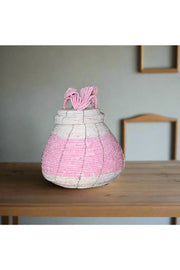 Hand holding a pink and gray beaded container with a blurred background