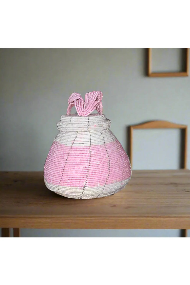 Hand holding a pink and gray beaded container with a blurred background