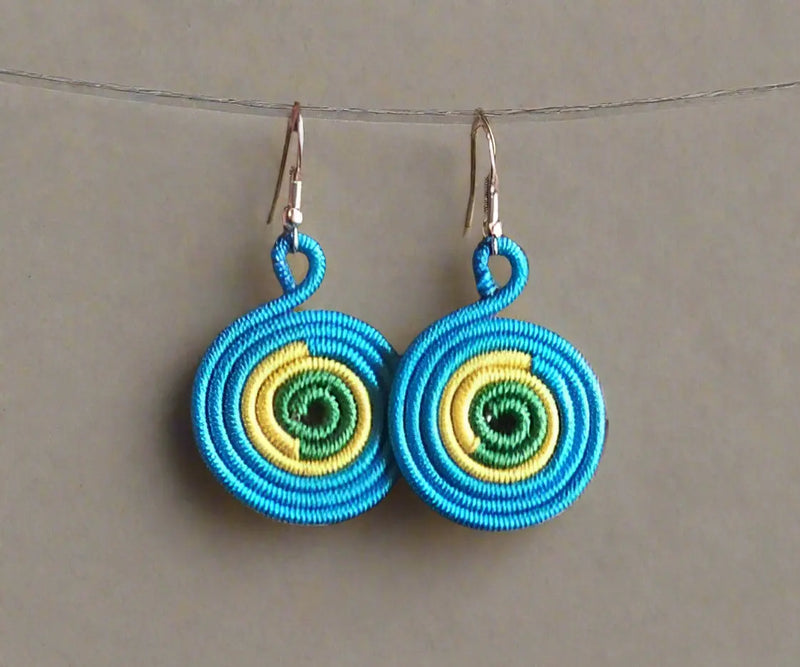 Hand holding a pair of colorful circular earrings with a background of more jewelry.