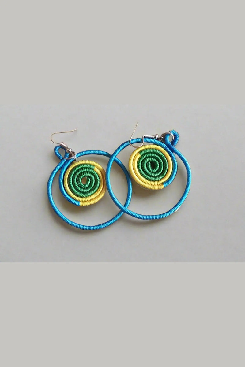 Colorful spiral earrings held in a hand with a background of more earrings on a board.
