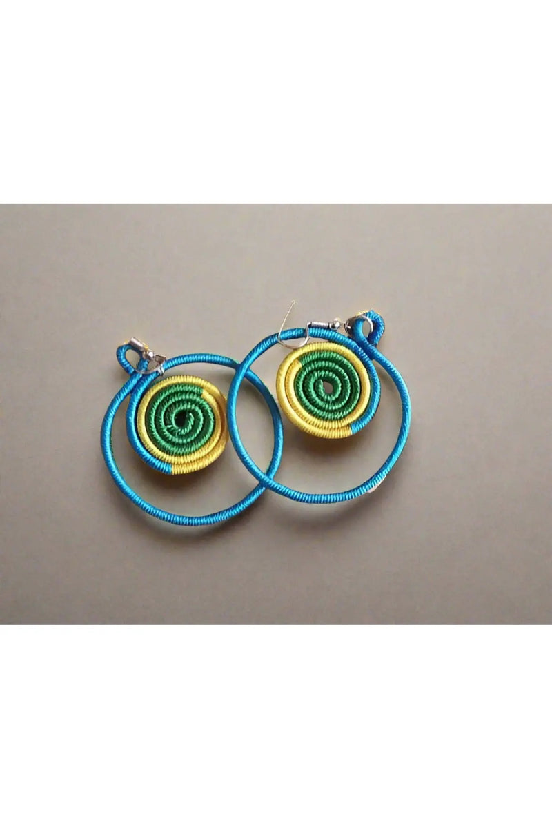 Colorful spiral earrings held in a hand with a background of more earrings on a board.