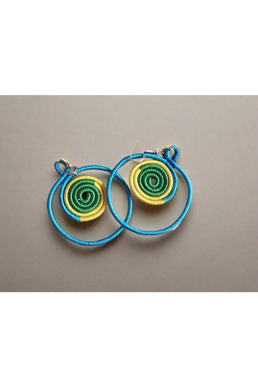 Colorful spiral earrings held in a hand with a background of more earrings on a board.