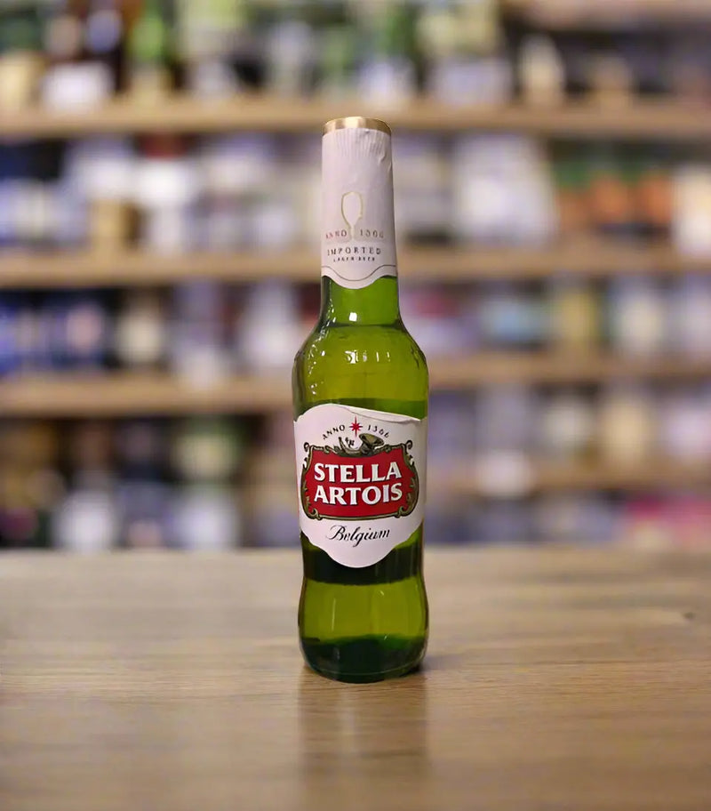 Stella Artois beer bottle held by a hand on a tiled floor with a store aisle in the background